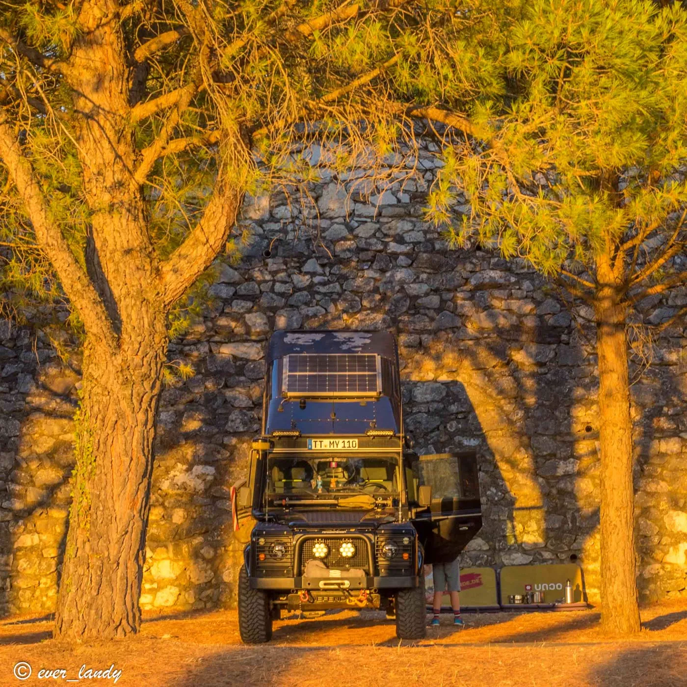 Night camp under illuminated trees next to an old stone wall