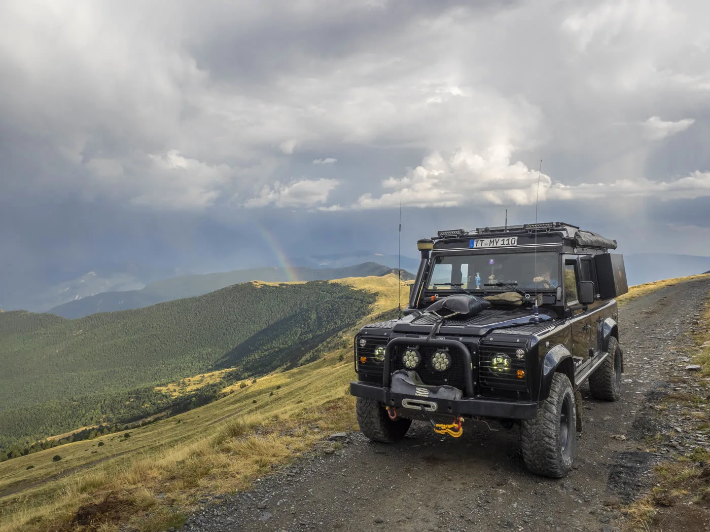Defender on a mountain ridge with a rainbow in the valley